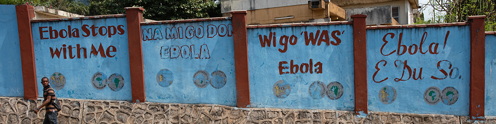 Photo showing 'Ebola Stops With Me' in different languages on a roadside.