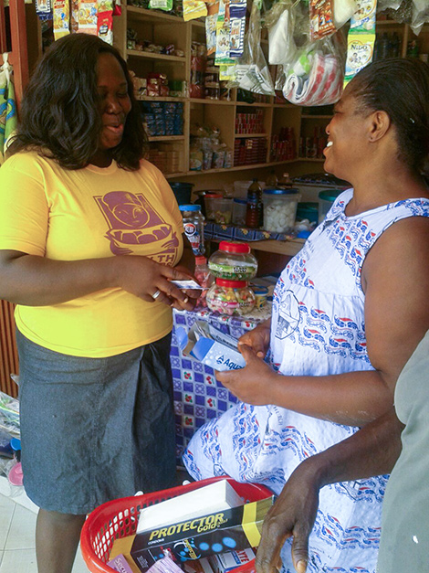 Photo of HealthKeeper Getrude Kofie speaking to a shopkeeper.