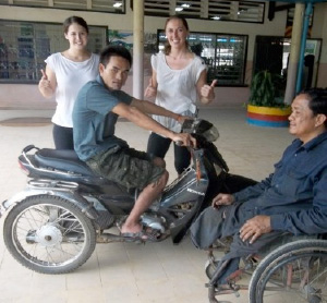 Photo of Hoeun Chan on a motor scooter with two women giving thumbs up in background