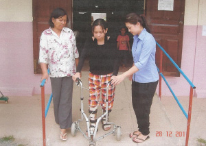 Photo of Ros Sokhom using a wheeled walker flanked by two women