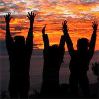 Photo of people with their arms raised at sunset