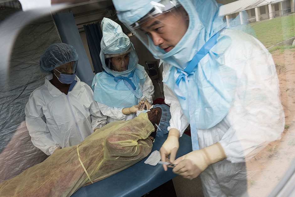 Photo of two doctors and an assistant in protecting gear and working inside the Pod, with a patient lying between them.