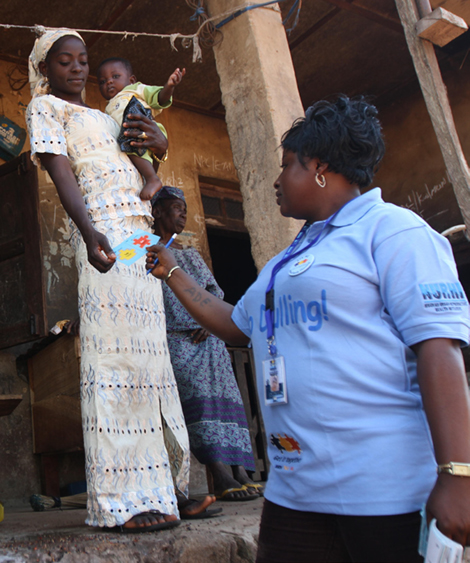 Photo of a female health worker handing a Go card to a woman outside her home