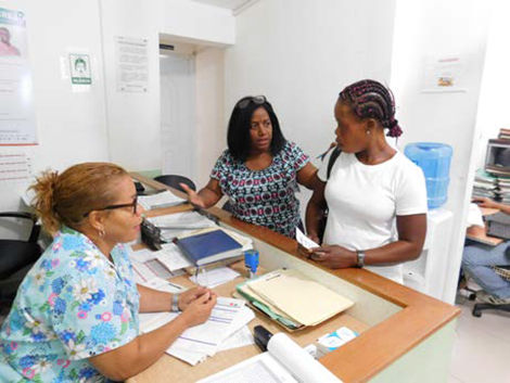 Photo of a navigator with a woman at a clinic counter and a nurse.