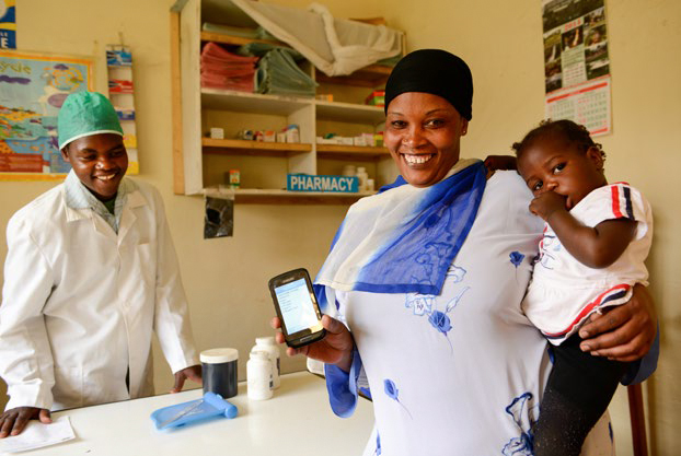 Photo of a woman at a health clinic holding a smartphone and an infant.